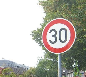 Ein Verkehrsschild an einer Straße. Auf dem Schild steht 30 und weist auf das Tempo Limit hin.