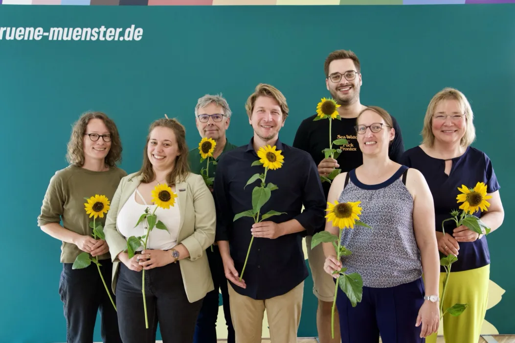 Auf dem Bild stehen Sonja Völker, Katie Foreman, Fritz Bachmair, Jörg Rostek, Lukas Färber, Birgit Wolters und Almut Wiemers vor einem Grünen Hintergrund