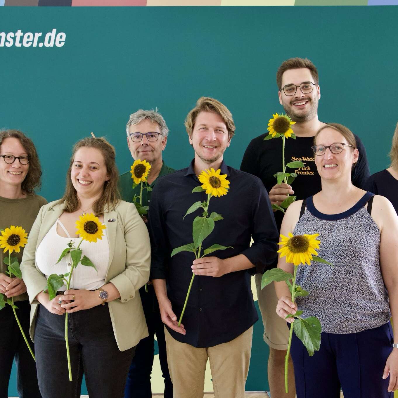 Auf dem Bild stehen Sonja Völker, Katie Foreman, Fritz Bachmair, Jörg Rostek, Lukas Färber, Birgit Wolters und Almut Wiemers vor einem Grünen Hintergrund