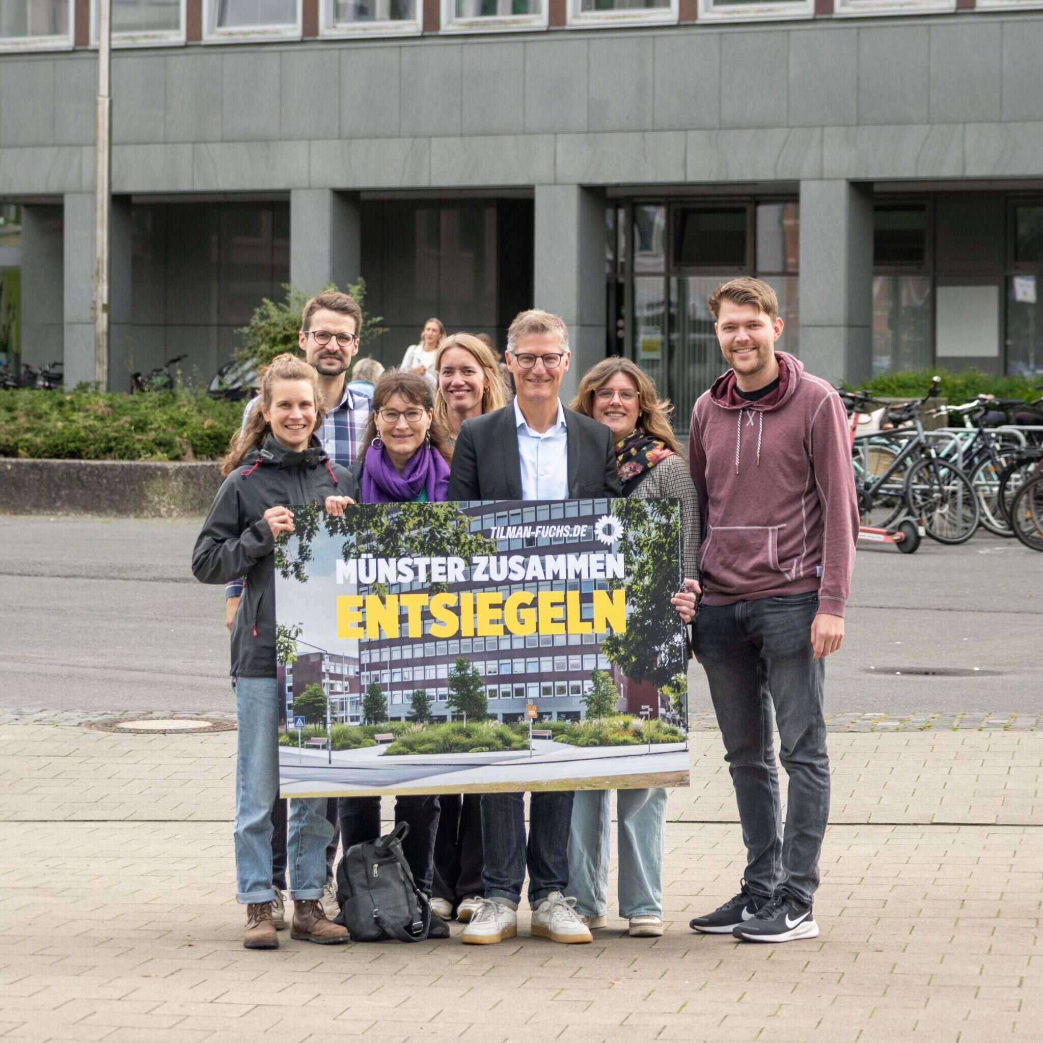 Die Grünen Kandidat*innen mit einem KI-Foto der Entsiegelung vor dem Stadthaus 2