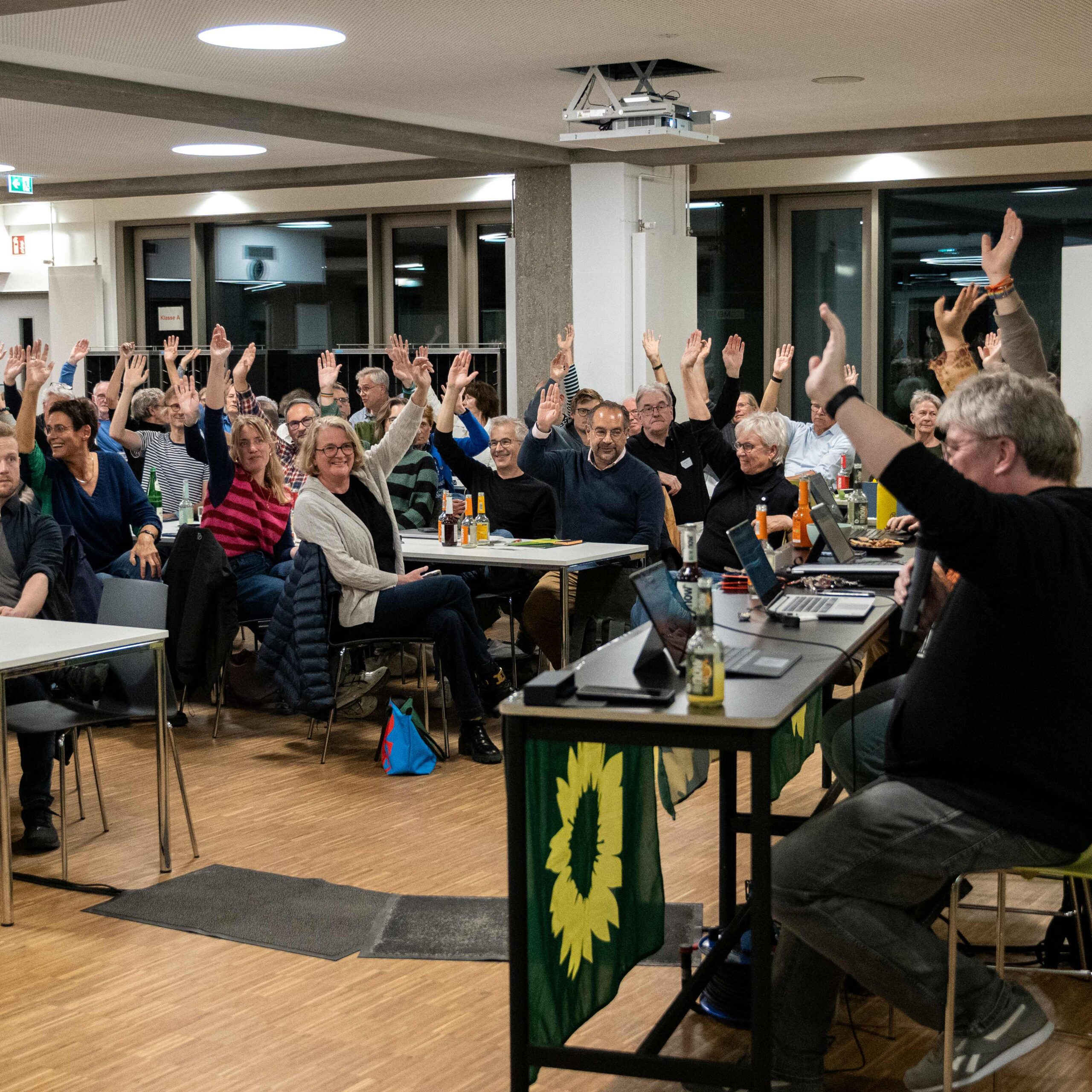 Menschen auf der Mitgliederversammlung heben die Hand für eine Abstimmung
