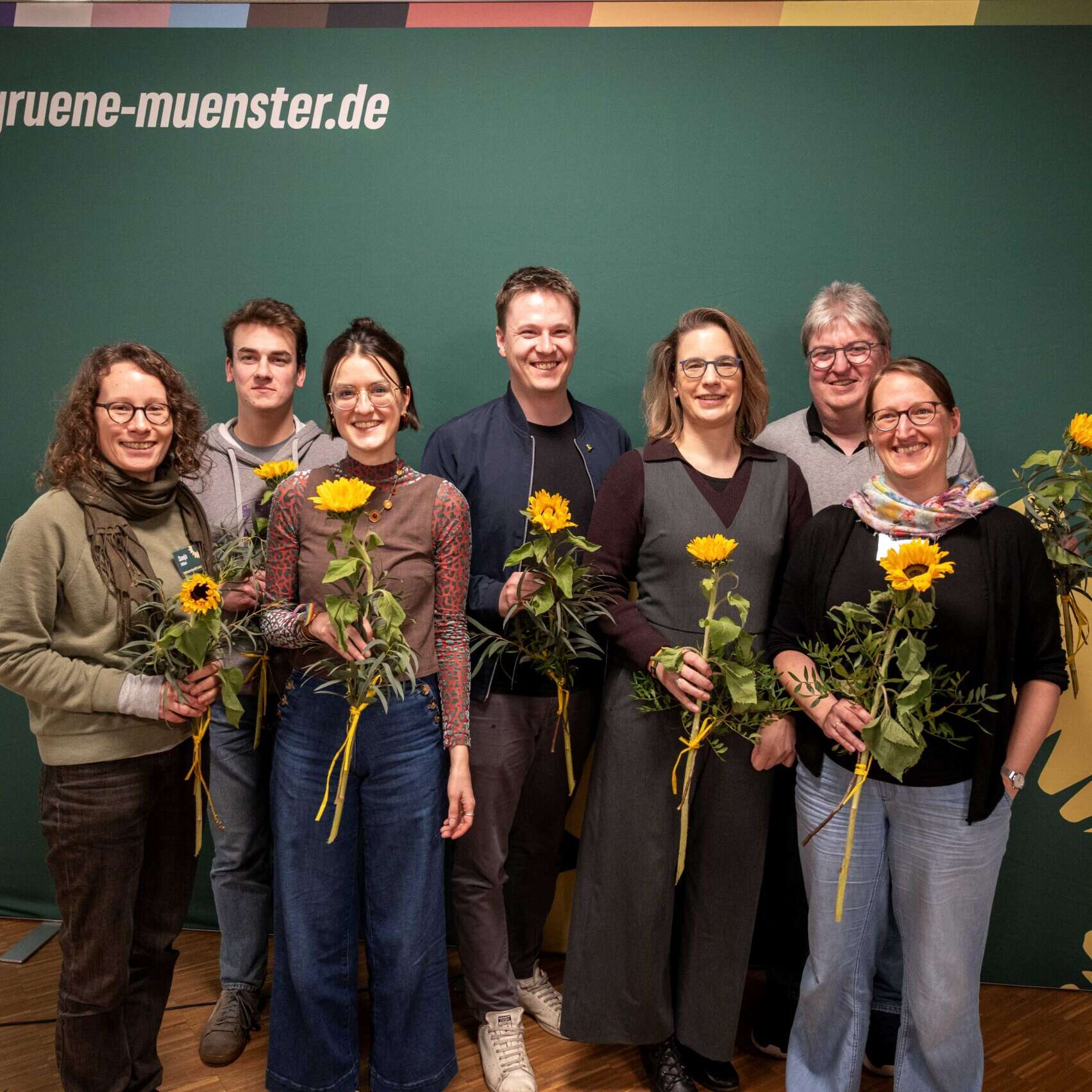 Der neue Vorstand steht vor einem Grünen Hintergrund und hält Sonnenblumen in der Hand